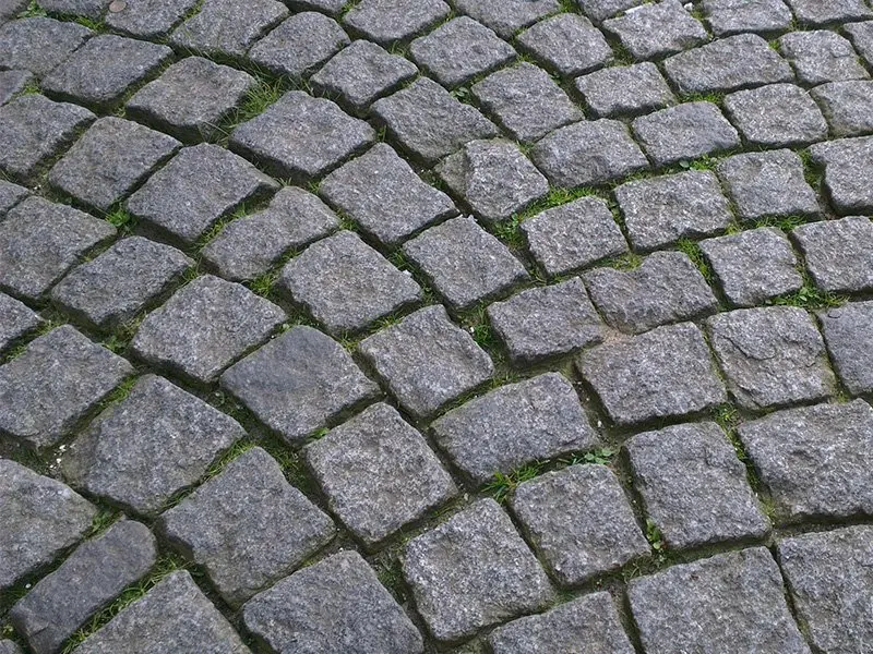 Granitpflaster mit halb leeren Fugen, in denen Gras wächst