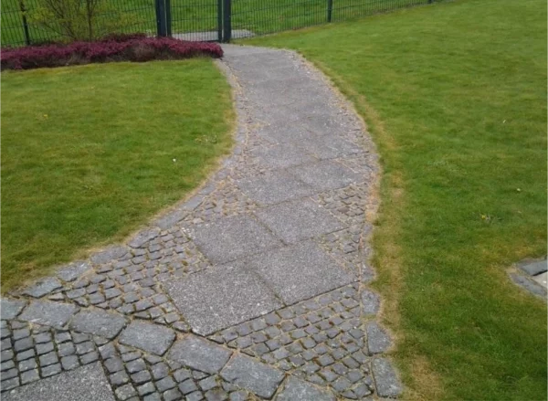 Weg aus wei&szlig;en Granitplatten mit Kopfsteinrand, stumpf und grau-braun verschmutzt